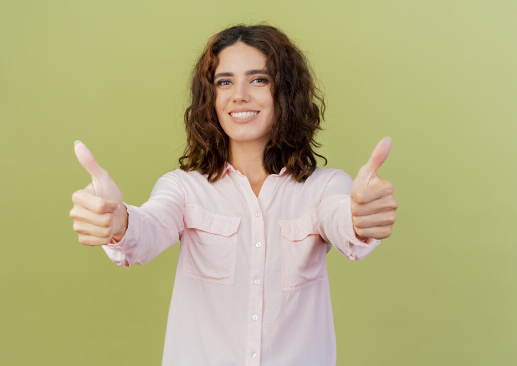 smiling young caucasian girl thumbs up with two hands isolated on green background with copy space