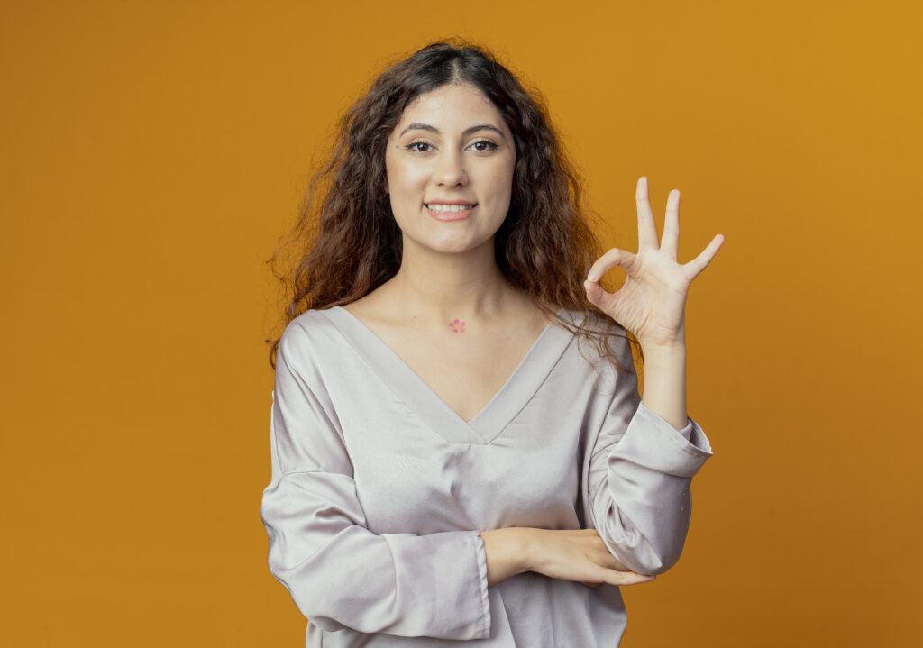 smiling young pretty girl showing okey gesture isolated on yellow background